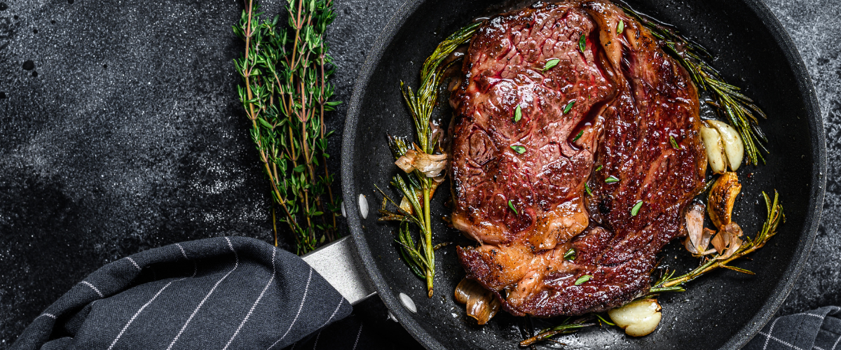 overhead view of a cooked steak in a pan on a grey surface